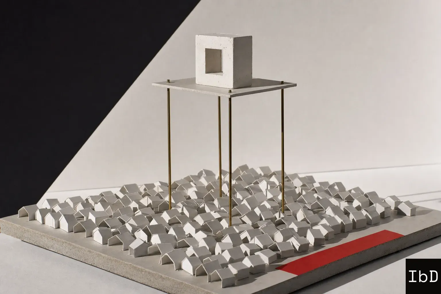 An architectural study model showing a vast lower grid of tiny folded paper houses, with a single white plaster block held high above them on a rigid platform supported by tall brass rods.