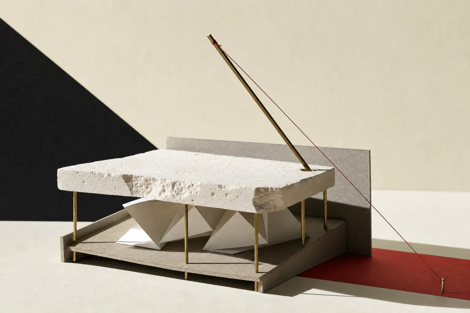 A physical study model made of plaster, card, and brass rods featuring folded paper forms suspended inside a hollow space below a thick plaster slab.